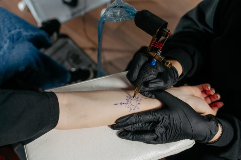 An artist draws a tattoo on a client’s forearm