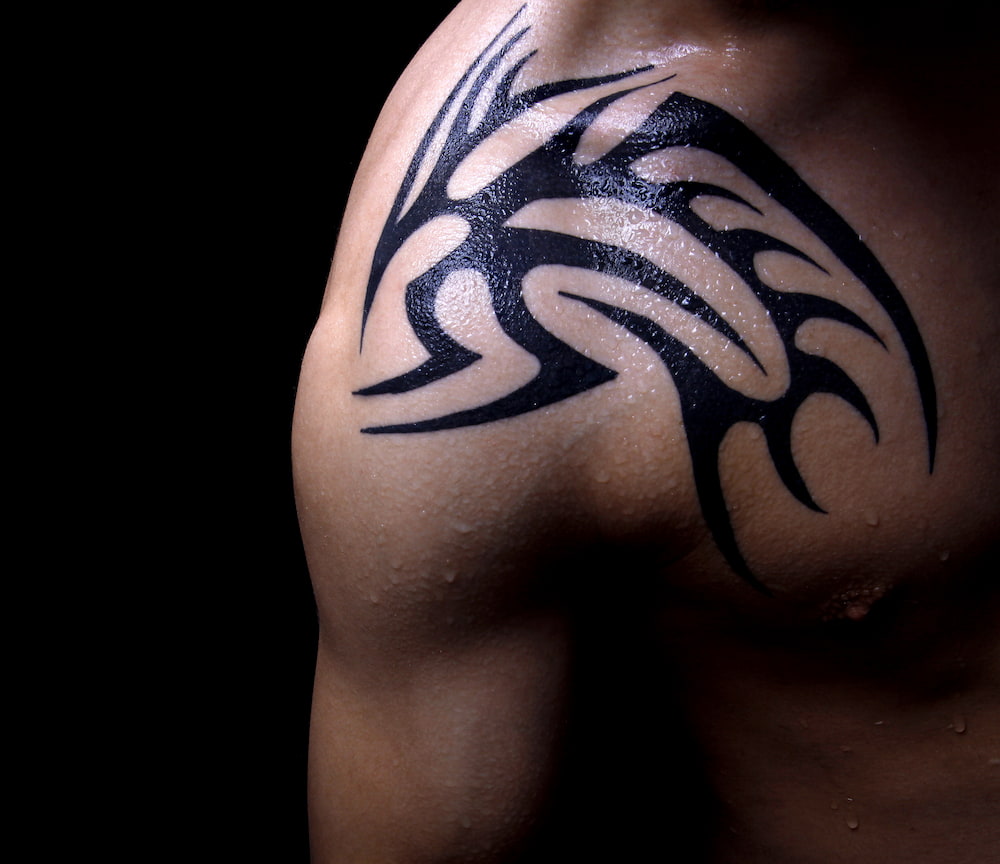 a man’s shoulder with a vivid black tribal tattoo covered in a layer of sweat the image is not right for the content